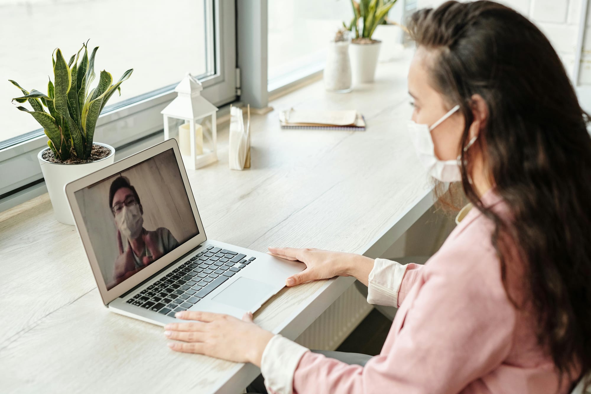 Woman having a telehealth consultation on her laptop, both wearing masks for health safety